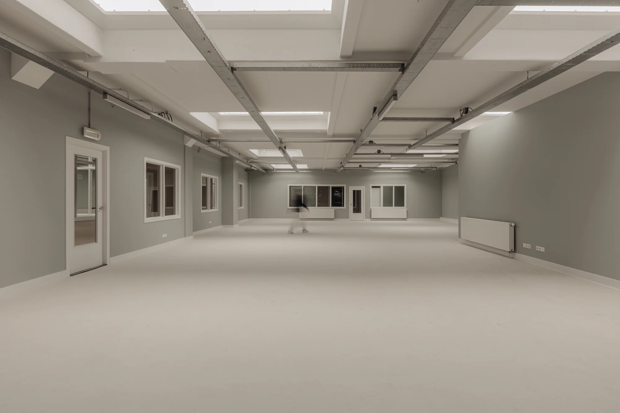 Ruime, lege kantoorruimte aan de Henri Polaklaan met grijze muren, witte deuren en ramen, en zichtbare plafondconstructie.